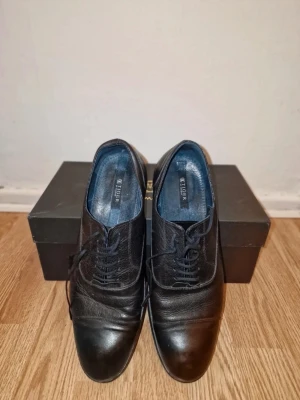 Svarta finskor från Tiger of Sweden - Klassiska svarta loafers från Tiger of Sweden i skinn med rund tå och diskreta sömdetaljer. Snygg och tidlös modell som passar till många olika stilar. Skorna har låg klack och platt sula.