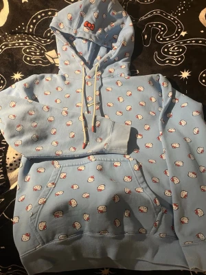 Blå Hello Kitty x Nike hoodie - Säljer en ljusblå hoodie från Nike med Hello Kitty-mönster över hela tröjan. Hoodien har huva med dragsko, magficka och broderad Nike-logga framtill. Perfekt för dig som gillar unika samarbeten och gulliga detaljer. Använd kanske 1-2 gånger så praktiskt taget i nyskick 