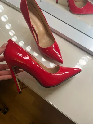 Röda lackade pumps med spetsig tå - Snygga röda pumps i glansigt lackmaterial med spetsig tå och hög klack. Klassisk och elegant design som ger en riktigt statement-look. Perfekta för dig som vill sticka ut och addera färg till outfiten.