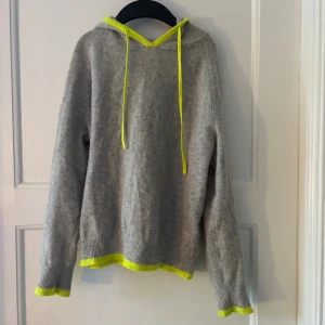 From future hoodie -  grå hoodie med neon-gula snören samt kanter vid ärmslut och nederkant. Den är i Kashmir och har ett litet håll (se på bild) på luvan men inget märkbart