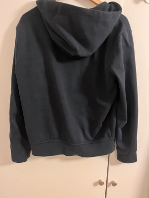 Mörkblå hoodie från Polo Ralph Lauren - Snygg mörkblå hoodie från Polo Ralph Lauren med dragkedja, huva och snörning. Tröjan har långa ärmar, två fickor fram och den klassiska Polo-loggan broderad på bröstet. Perfekt för chill dagar och enkel att matcha med jeans eller joggers. Hör av er vid minsta fundering🙌🤝