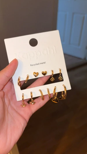 Guldiga örhängen  - Säljer ett set med guldiga örhängen från Kappahl i återvunnet metall. Setet innehåller flera olika modeller, bland annat små hjärtan, ringar och stjärnor. Perfekt för att mixa och matcha till olika looks. Alla örhängen är i en snygg guldfinish. Allt är oanvänt. Perfekt till julklappspel!!Nypris 129kr