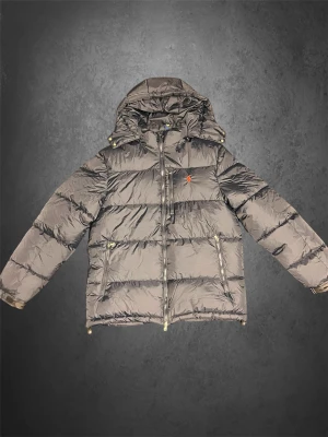 Svart pufferjacka från Polo Ralph Lauren - Svart pufferjacka från Polo Ralph Lauren Jackan har det klassiska röda Polo-logot broderat på bröstet och två sidofickor med dragkedja. Materialet är glansigt och syntetiskt, perfekt för kalla dagar.