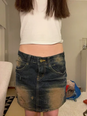 Mörkblå y2k vintage jeanskjol  - Säljer en mörkblå jeanskjol med slitna detaljer och coola bruna partier. Kjolen är kort, har klassiska fickor fram och bak samt synliga sömmar i kontrastfärg. Perfekt för dig som gillar en edgy och avslappnad stil. Knappast använd och i fint skick. Själv är ca 152cm och kjolen är ganska lång på mig.  ✔️ Mått: Ungefär 37cm ➡️midja                Ungefär 33cm ⬇️längd ✔️ Färg: Mörkblå, brun, guld.