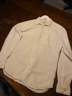 Beige linneskjorta från East West - Snygg beige skjorta från East West i ren linne, regular fit. Klassisk design med krage, bröstficka och knappar framtill. Perfekt för dig som gillar en clean och chill stil. Långärmad och lätt material som passar när du vill vara bekväm men ändå se fräsch ut. 