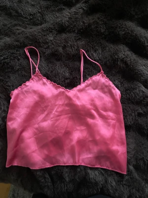 Rosa satin linnetopp från Bershka - Säljer en rosa linnetopp från Bershka i satinliknande material. Toppen har tunna axelband och en lätt vågig kant vid urringningen. Perfekt för dig som gillar en enkel men ändå snygg look. Storlek XS.