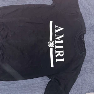 Svart AMIRI t-shirt med tryck - Säljer en svart t-shirt från AMIRI med stort vitt logotryck på bröstet. Klassisk rund hals och korta ärmar. Perfekt för dig som gillar streetwear och vill ha en enkel men snygg look.