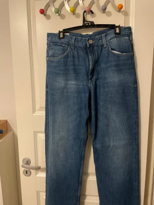 Blå jeans med raka ben -  Blåa baggy jeans med raka ben. Kan spännas åt med hjälp av det som sitter på bak