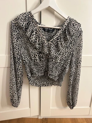 Leopardmönstrad blus från Zara XS - Snygg blus från Zara i leopardmönster med volangdetaljer vid halsen och smockad midja. Långärmad modell i lätt, skrynkligt tyg som ger en cool och trendig vibe. Perfekt för dig som gillar att sticka ut med djurmönster och volanger.