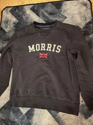 Morris sweatshirt mörkblå - Morris sweatshirt i mörkblå färg. Tröjan har använts i nästan ett år men är fortfarande i mycket bra skick. Storlek M. Materialet är mjukt och bekvämt, och passformen är klassisk. Passar bra för personer som är ca 175 cm. Perfekt för både vardag och lite mer uppklädda tillfällen. Vid snabb affär kan priset sänkas