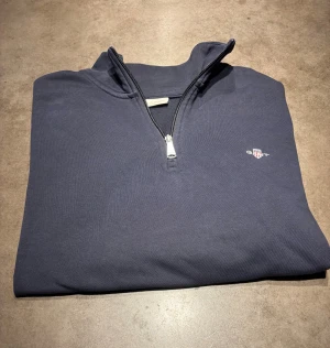 GANT Quarter Zip - Säljer en snygg Marin Blå Gant Quarter Zip. Snygg, skönt material på insidan och stilren. långärmad tröja från GANT med Quarter zip och stilren. Storlek: L. Skriv vid frågor eller kom med bud!