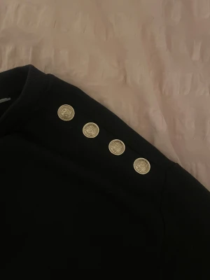 Svart tröja med guldknappar - Säljer en svart tröja med fyra snygga guldknappar på. Perfekt för dig som vill ha en skön men ändå uppklädd stil.