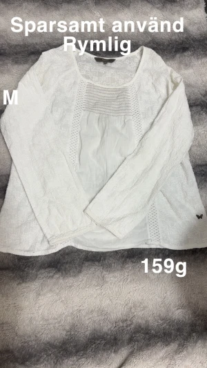 Vit spetsblus, M - Säljer en vit blus med långärmade ärmar och snygga spetsdetaljer. Blusen har rund halsringning och ett luftigt, rymligt snitt. Materialet är lätt och har ett diskret mönster samt en liten fjärilsdetalj nedtill.🌸 Sparsamt använd. Storlek M men rymlig.