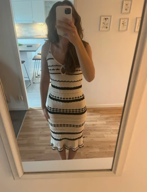 Virkad beige klänning med svarta detaljer - Klänningen har justerbara band och är virkad med olika mönster samt har volanger längst ner.