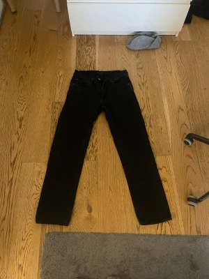 Svarta jeans från Nudie Jeans, 29/30 - Säljer ett par svarta jeans från Nudie Jeans i storlek 29/30. Klassisk femficksmodell med raka ben och diskret Nudie-lapp bak i midjan. Jeansen har en clean look och är tillverkade i mjukt bomullstyg för skön passform.