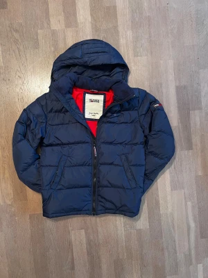 Mörkblå dunjacka Tommy Hilfiger - Snygg marinblå pufferjacka från Tommy Hilfiger Denim med huva och dragkedja. Perfekt för kalla dagar och riktigt skön att bära ❄️.  Skick 9/10 ✅ Nypris cirka 2500 Skickar inom 48 timmar om inte samma dag 🚚