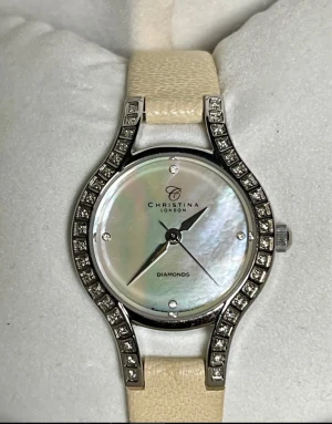 Christina London diamantklocka pärlemor - Lyxig damklocka från Christina London med äkta diamanter (0,11 ct), pärlemor-urtavla och glittrande stenar runt boetten. Beige läderarmband och silverfärgad boett. Levereras i hjärtformad originalask. Swiss made.