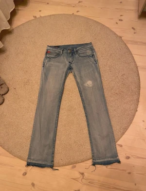  ljusblå Lee jeans med slitningar - Säljer ett par ljusblå jeans från Lee Cooper som är uppsprättade där nere. Modellen har klassiska fem fickor, kontraststickningar och en liten röd detalj vid fickan. Jeansen har rak passform och låg midja.   Använd en gång och det var av den tidigare säljaren. Säljs pga fel storlek.                           Midjemått: 39cm rakt över                                          innebenslängd: 75cm                                                    bredd vid lår: 23cm