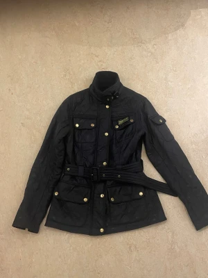 Svart quiltad jacka från Barbour - Svart quiltad jacka från Barbour International med gulddetaljer, bälte i midjan och flera fickor med tryckknappar. Jackan har hög krage, dragkedja och långa ärmar med snygga detaljer. Perfekt för dig som gillar klassisk stil med edge. Fungerar väldigt bra, skriv ifall du har fler frågor eller vill ha mer info. ABS! Pris går att diskutera.