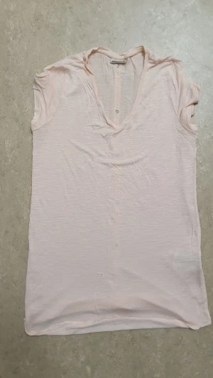 T-shirt - Ljusrosa t-shirt från H&M i mjuk bomull. Modellen är ärmlös med v-ringning och dekorativa knappar längs ryggen. Perfekt för en avslappnad och stilren look. Tunt och svalt material som passar bra till varmare dagar.