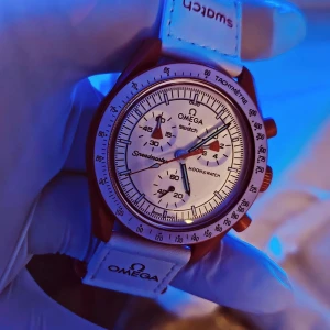 OmegaxSwatch - Speedmaster MoonSwatch - Mission to Mars - Helt ny Omega x Swatch MoonSwatch Speedmaster - Mission to Mars i låda inkl. allt. Endast använd 1 gång för foto. Klockan är helkeramisk och har vit urtavla med röda och gröna visare, tachymeter-skala och flera subdials. Vitt läderarmband med Omega-logga och texten Speedmaster undertill. 