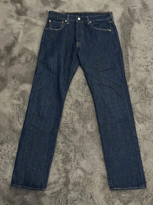 Levi's 501 mörkblå jeans 32/32 - Klassiska Levi's 501 jeans i mörkblå denim med raka ben och femficksmodell. Byxorna har gul kontrastsöm, knappgylf och ikonisk läderpatch bak i midjan. Perfekta för dig som gillar tidlös stil och vill ha ett par jeans som funkar till allt.