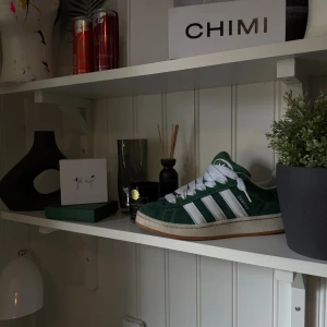 Adidas Campus gröna sneakers - Gröna Adidas Campus sneakers med klassiska vita ränder på sidan och vit logga på tungan. Skorna har en låg profil, rund tå och platt sula i gummi. Ovandelen är i mjuk mocka med vita snören och detaljer. Perfekt för dig som gillar retrostil och streetwear. Box fårs med också. 