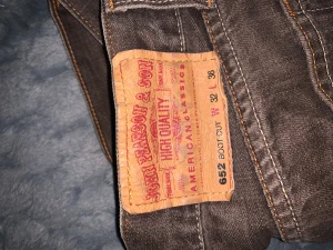 Bruna bootcut jeans från John Pearson & Son - Snygga bruna jeans från John Pearson & Son i bootcut-modell. Klassisk femficksdesign med kontrastsömmar och läderpatch bak. Jeansen är tillverkade i slitstarkt denim och har en cool vintagekänsla. Perfekt för dig som gillar avslappnad stil. Lite slitna längst ner vid bena i hällarna 