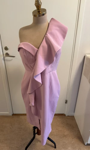 Ljuslila one shoulder klänning Lavish Alice - Superfin ljuslila klänning från Lavish Alice med en axel och volangdetalj. Figurnära passform, slits framtill och dragkedja i sidan. Perfekt för dig som vill sticka ut med en elegant och modern look. Materialet känns mjukt och har en lätt glans.