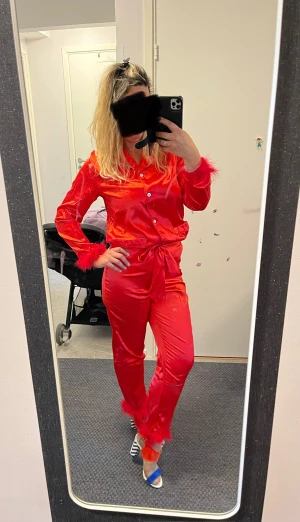 Röd pyjamas med fjädrar - Säljer en röd pyjamas med skjorta och byxa. Skjortan har knappar och krage, byxan har midjeband med knyt.  Perfekt för pyjamas party eller sexigt look 