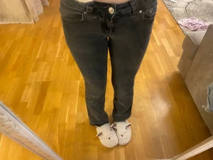 Svarta jeans från Perfect Jeans - Snygga svarta jeans från Perfect Jeans med låg midja och raka ben. Jeansen har klassiska fem fickor, silverfärgade knappar och detaljerade bakfickor med lock. Materialet är stretchigt jeans för en bekväm passform.