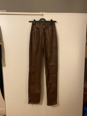 Bruna skinnbyxor, Design by Si - Bruna skinnbyxor från Design by Si med hög midja och raka ben. Byxorna har klassiska fickor fram och bak, vita kontrastsömmar och kort slits vid benslut. Aldrig använda