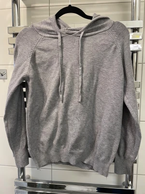  Grå Kashmir hoodie  - Mysig grå hoodie i stickat material med huva och dragsko. Tröjan har ribbade muddar vid ärmslut och nederkant, samt raglanärmar för en avslappnad vibe. Perfekt för chill dagar och enkel att matcha med jeans eller mjukisbyxor.