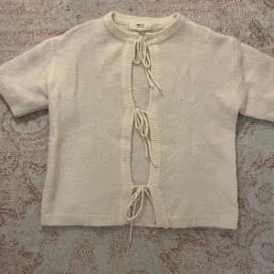 Vit kortärmad kofta från Gina Tricot - Superfin vit kofta från Gina Tricot i ullblandning. Kortärmad modell med 3 rosetter framtill. Går att styla åt båda hållen