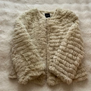 Beige pälsjacka från Trilogy Collections - Supermjuk och fluffig beige pälsjacka från Trilogy Collections. Perfekt för dig som vill sticka ut med en lyxig vibe och hålla dig varm under kyliga dagar.