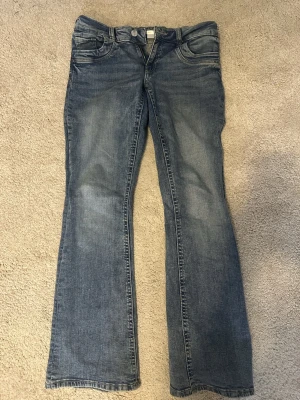 Blå bootcut jeans med slitningar - Snygga blå bootcut jeans med lätt slitna detaljer och klassisk femficksdesign. Jeansen har normal passform och är tillverkade i mjukt denimtyg av bomull. Perfekta för dig som gillar en avslappnad men ändå trendig look.