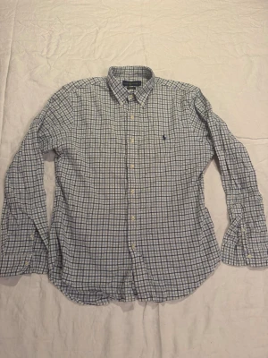 Rutig skjorta från Ralph Lauren - Snygg rutig skjorta från Ralph Lauren i blått och vitt. Slim fit-modell med button-down krage och klassisk broderad logga på bröstet. Tillverkad i stretchig oxford-bomull för extra komfort. Perfekt till jeans eller chinos.
