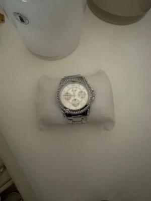 Silvrig klocka från Regal - Stilren klocka från Regal med länkarmband i silverfärgat metall. Klassisk design som passar till många olika stilar. Låset är graverat med Regal-loggan och armbandet har en snygg, polerad finish. Extra länkar medföljer! Obs batteriet behöver bytas🤎