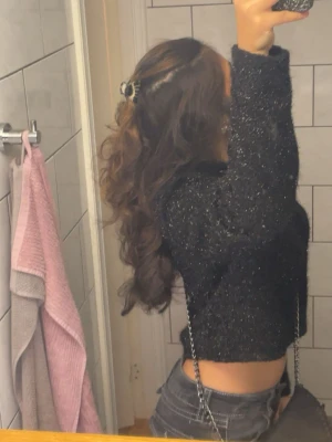 Glittrig svart cropped stickad tröja - Snygg svart stickad tröja med glittriga inslag och cropped passform. Tröjan har långa ärmar och en trendig, lite lös siluett. Perfekt för att lyfta en outfit med lite extra bling.