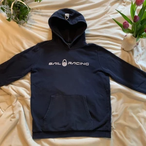 Mörkblå hoodie från Sail Racing - Säljer en snygg mörkblå hoodie från Sail Racing med vit logga på bröstet. Tröjan har en klassisk känguruficka och en bekväm huva med logga. Perfekt för en avslappnad stil. Storleken är 170 . Skriv till mig vid minsta fråga jag svarar snabbt. Priset kan diskuteras 