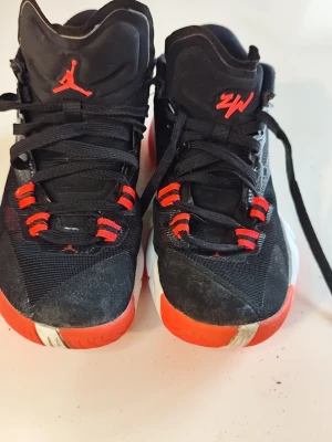 Svarta och röda Jordan sneakers - Snygga svarta och röda Jordan sneakers med högt skaft och klassisk Jumpman-logga på plösen. Skorna har svarta snören, röda detaljer och vit sula med röd kant. Ovandelen är i syntetmaterial med mesh och glansiga partier på sidan.Du är varmt välkommen att kika på mina andra annonser.