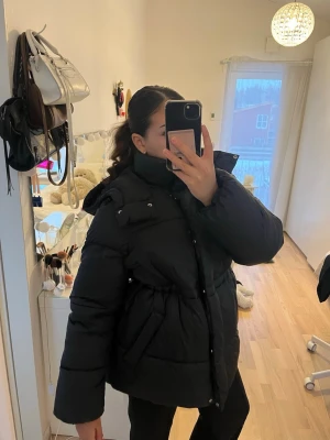 Svart pufferjacka med huva - Snygg svart pufferjacka med huva och markerad midja. Jackan har en oversized passform med långa ärmar. Strl S men passar även M. Perfekt för vintern!❄️