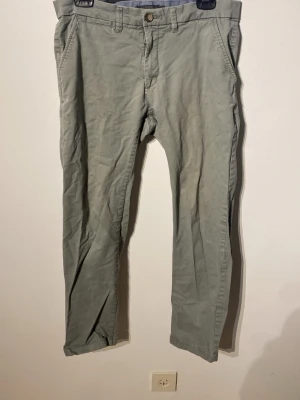 Gröna chinos med raka ben - Snygga gröna chinos med raka ben och klassisk passform. Byxorna har sidofickor fram, passpoalfickor bak med knapp och bälteshällor i midjan. Tillverkade i mjuk bomull. Lite urtvättade och det syns att de är använda.