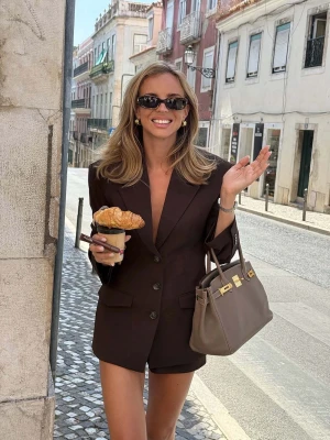 Brun oversized kavaj med knappar - SLUTSÅLD Lovisa Wallin x NAKD. Snygg mörkbrun oversized kavaj med klassisk krage och tre knappar framtill. Kavajen har långa ärmar och markerade axlar för en trendig siluett. Perfekt för dig som gillar en stilren och modern look.