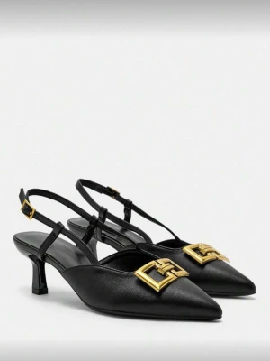 Svarta pumps med gulddetalj - Stilrena svarta pumps i skinn med spetsig tå och låg klack. Skorna har en elegant guldfärgad metallspänne framtill och justerbar rem runt hälen. Perfekta för dig som vill ha en klassisk men trendig look.