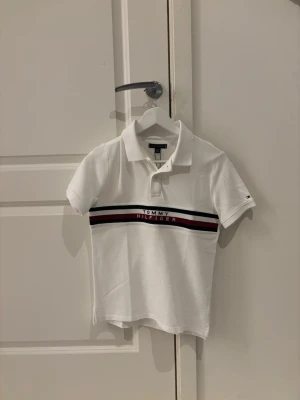 Vit Tommy Hilfiger piké - Tja. Säljer denna helt nya vita Tommy Hilfiger pikén. Den är i storlek 12-14 men passar XS. Bara testad en gång.