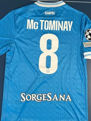 Napoli Fotbollströja McTominay #8 - Snygg Napoli matchtröja i blått med vita detaljer, tryck av McTominay och nummer 8 på ryggen. Champions League-märke på ärmen. Storlek M. Helt ny.