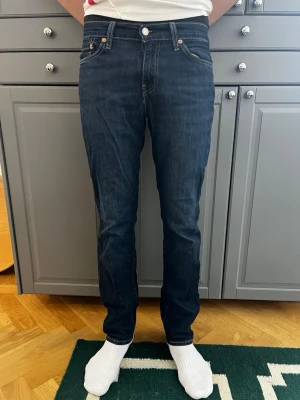 Mörkblå raka jeans från Levi's 511 - Säljer ett par klassiska mörkblå jeans från Levi's med rak passform och fem fickor. Modell 511. Stl W28, L33. Jeansen har kontrastsömmar och silverfärgade nitar. Perfekta till en avslappnad stil och funkar året runt.