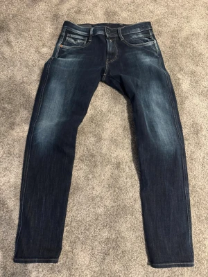 Replay Anbass blå jeans slim fit - Säljer ett par snygga Replay Anbass jeans i mörkblå tvätt med slitningar. Modellen har slim fit, klassisk femficksdesign och Replay-logga på myntfickan. Jeansen är tillverkade i stretchig bomullsdenim för skön passform. W28 L30, Skriv för frågor och lägg gärna bud!