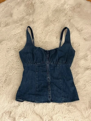 Hollister jeans topp  - Snygg mörkblå denim top med justerbara axelband och smockad rygg för extra komfort. Toppen har markerad midja och sömdetaljer framtill som ger en cool vintagekänsla. Perfekt att styla med jeans eller kjol för en trendig look.